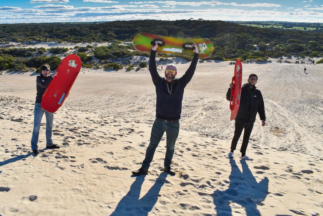 Intrepid travellers hold up boards ready for surfing the dunes at Little Sahara on Kangaroo Island