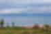 A set of yurts with one partially assembled sit on above the shore of Issy-Kul Lake with mountains in the distance