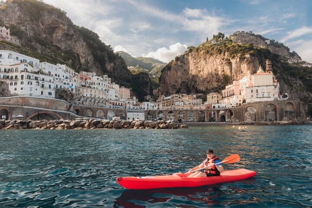 A traveller smiles as she kayaks along the Amalfi Coast with towering cliffs and colourful buildings