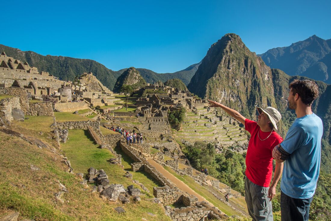Guide points to ruins of Machu Picchu in the distance while talking to traveller in Peru