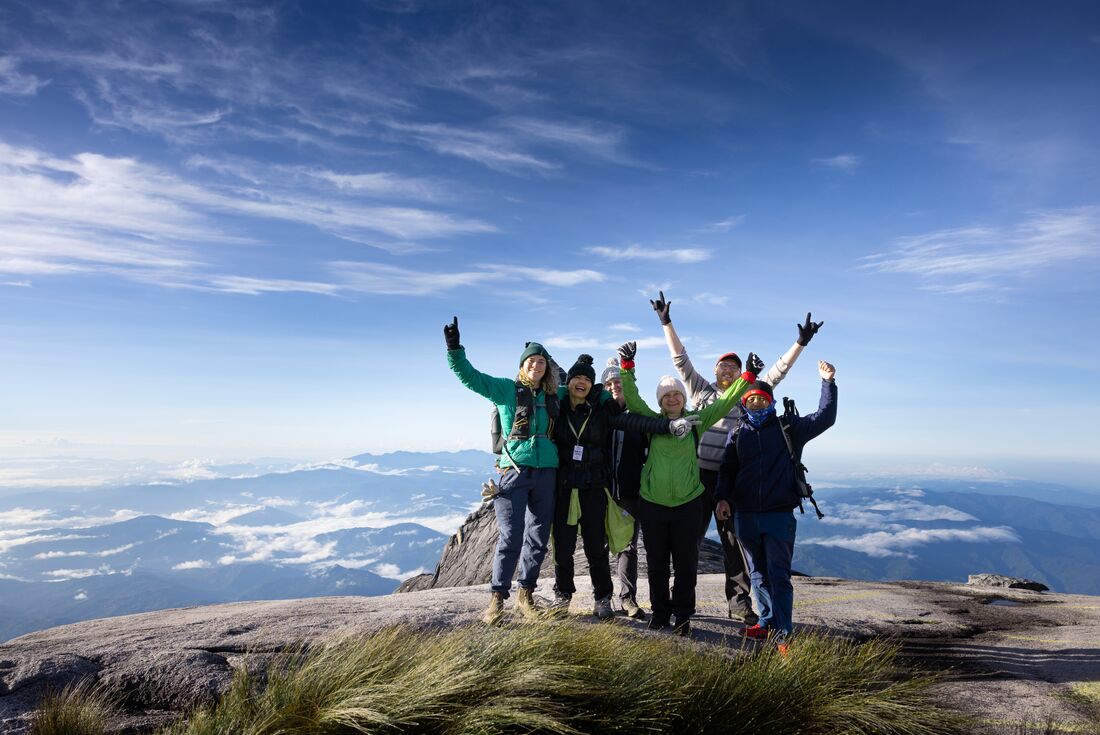 Intrepid Travellers throw their hands up as they take a group photo at the summit of Mount Kinabalu in Borneo