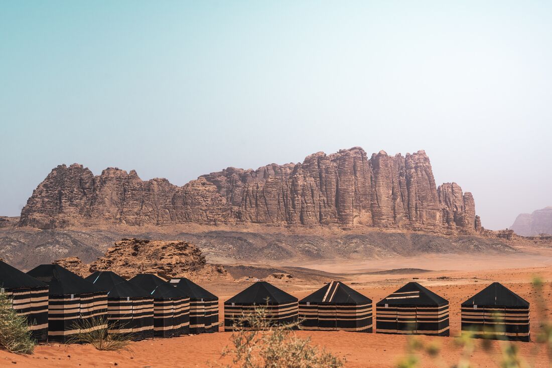 Wide view of black tents at Bedouin camp with mountain range in the background, Jordan