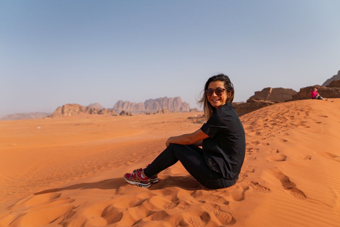 Smiling traveller sitting on sand dune in desert of Wadi Rum, Jordan