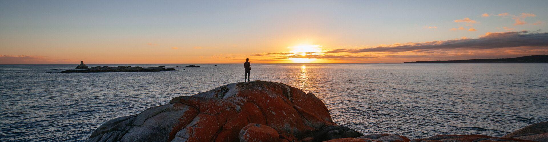 Silhouette of a person standing on a rock looking at the ocean at sunset