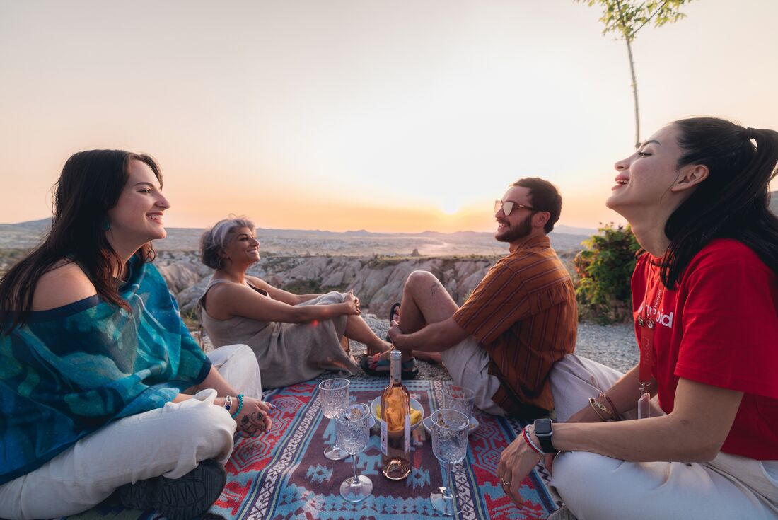 Leader and travellers enjoying wine at a picnic during sunset with a view of the valleys in Cappadocia, Turkey